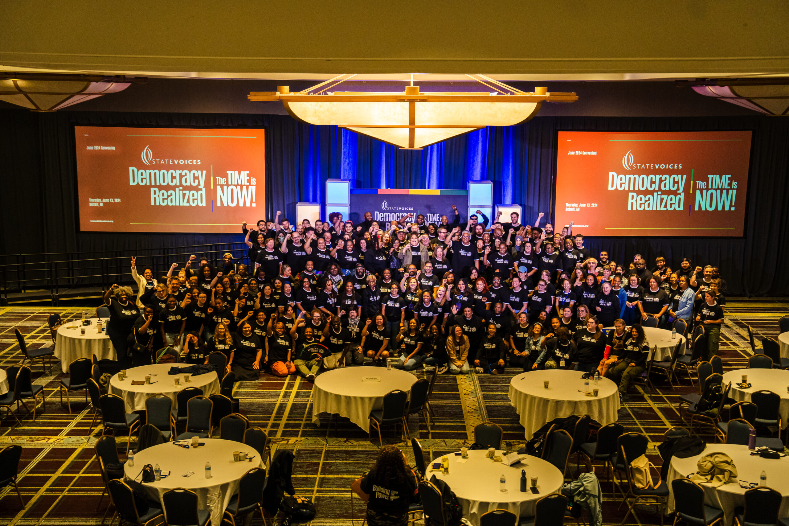 National Convening attendees pose for a group picture wearing matching black shirts with white words "Democracy Realized: The Time Is Now"
